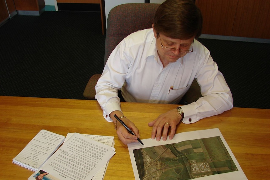 Mackay Canegrowers CEO Kerry Latter sits at a table with documents spread out in front of him.