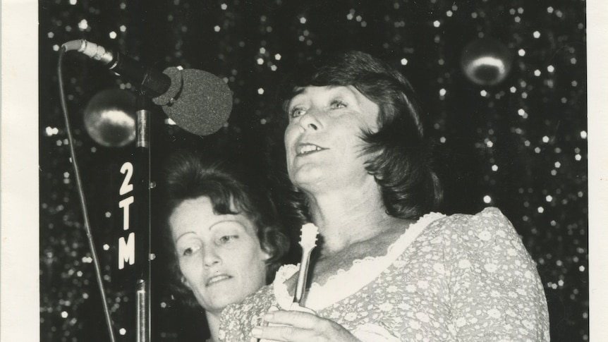 A black-and-white shot of a dark-haired, smiling woman – Joy McKean – accepting an award.