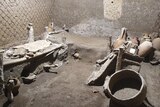 A room with several beds, amphoras and other items covered in residual volcanic ash.
