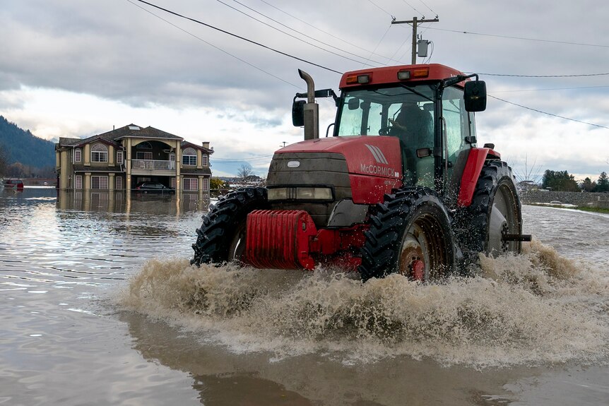 Czerwony traktor jedzie po zalanej drodze po ulewnym deszczu