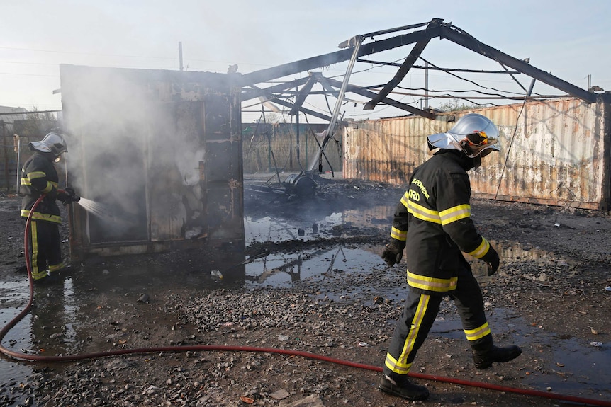 French firemen work near a burnt out shelter at the Grande-Synthe camp.