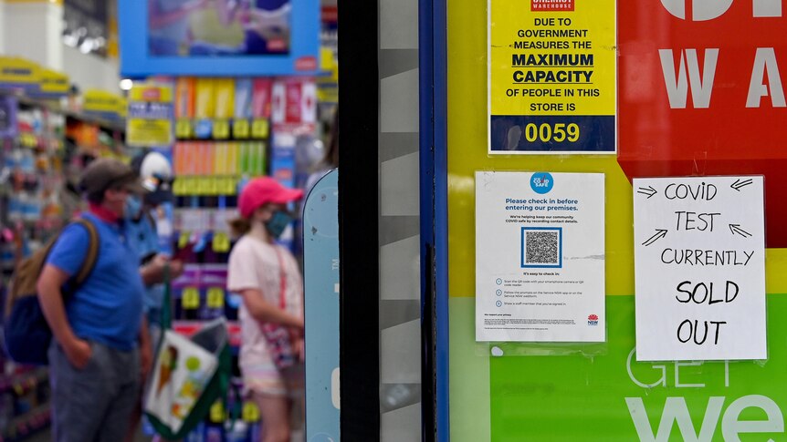 A sign outside a Chemist Warehouse says "COVID test currently sold out" as people queue in the background