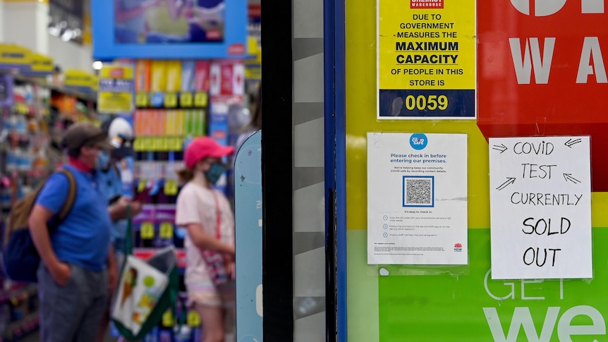 A sign outside a Chemist Warehouse says "COVID test currently sold out" as people queue in the background