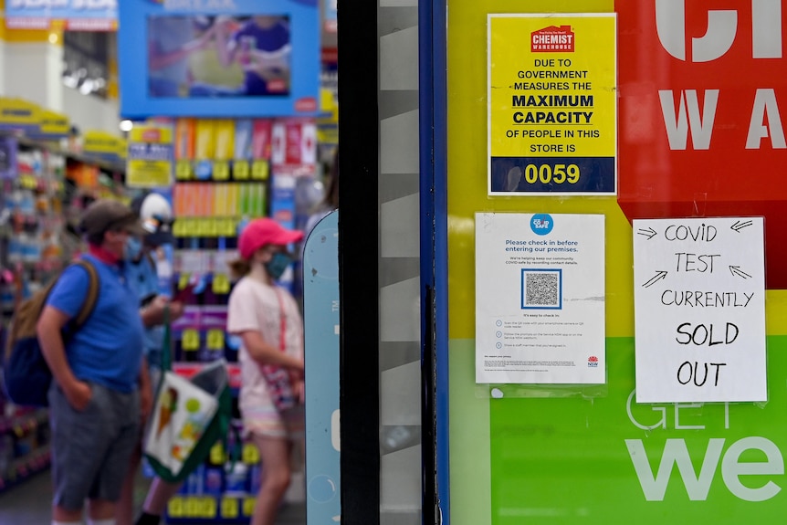 A sign outside a Chemist Warehouse says "COVID test currently sold out" as people queue in the background