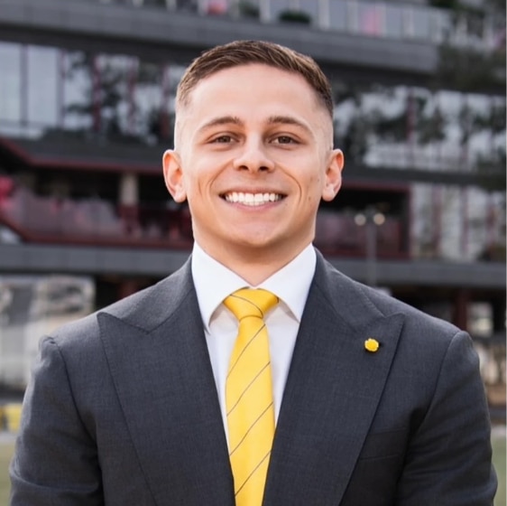 Homem de terno e gravata amarela sorri para a câmera.