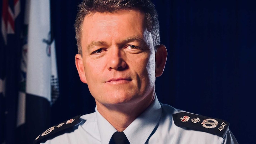 Australian Federal Police Commissioner Andrew Colvin in a dark room. He has an Australian flag and an AFP flag behind him.