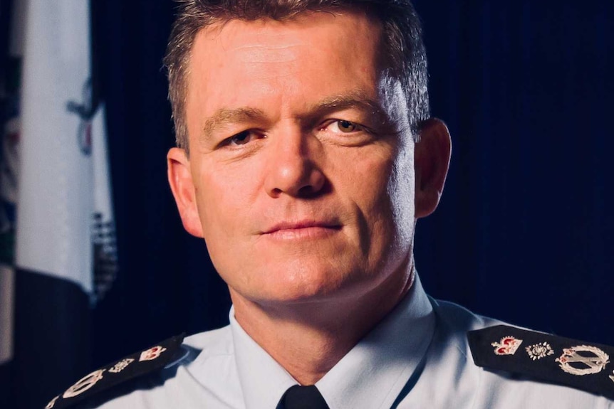 Australian Federal Police Commissioner Andrew Colvin in a dark room. He has an Australian flag and an AFP flag behind him.