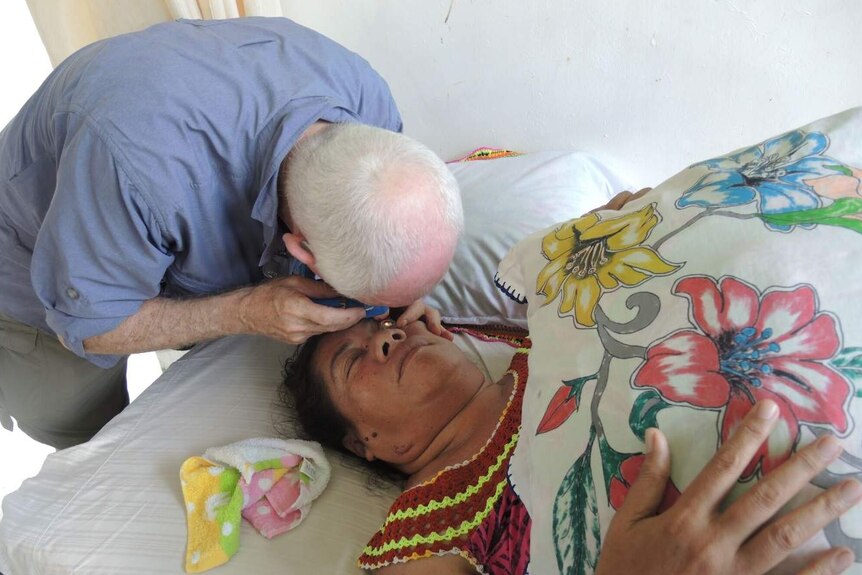 Patient lies on bed while doctor examines her eyes.