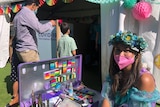 A female face painter in fancy dress sitting out the front of a white tent