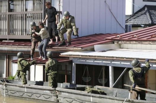 Military in boats assist stranded Japanese citizens from their houses.