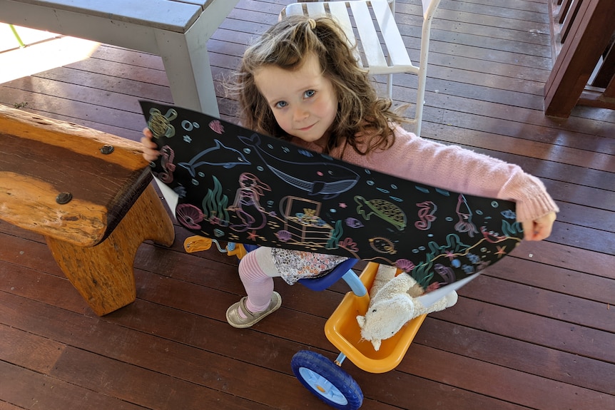 A little girl on a trike showing a picture of sea creatures.