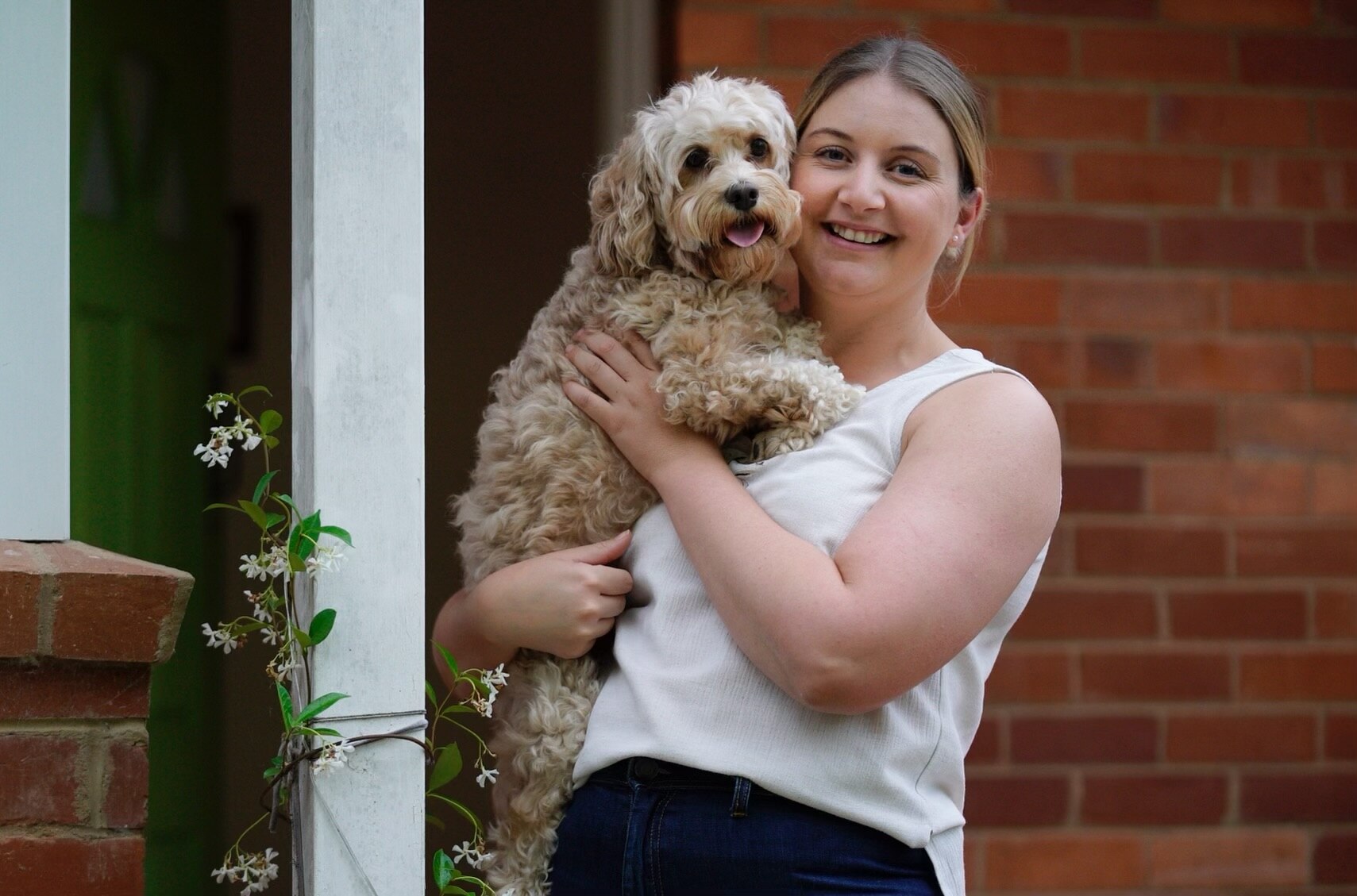 A blonde woman smiling and holding a cavoodle.