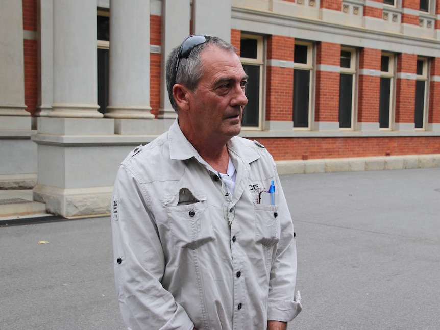 A middle-aged man with sunglasses on his head wearing a work uniform stands outside WA Supreme Court looking to one side.