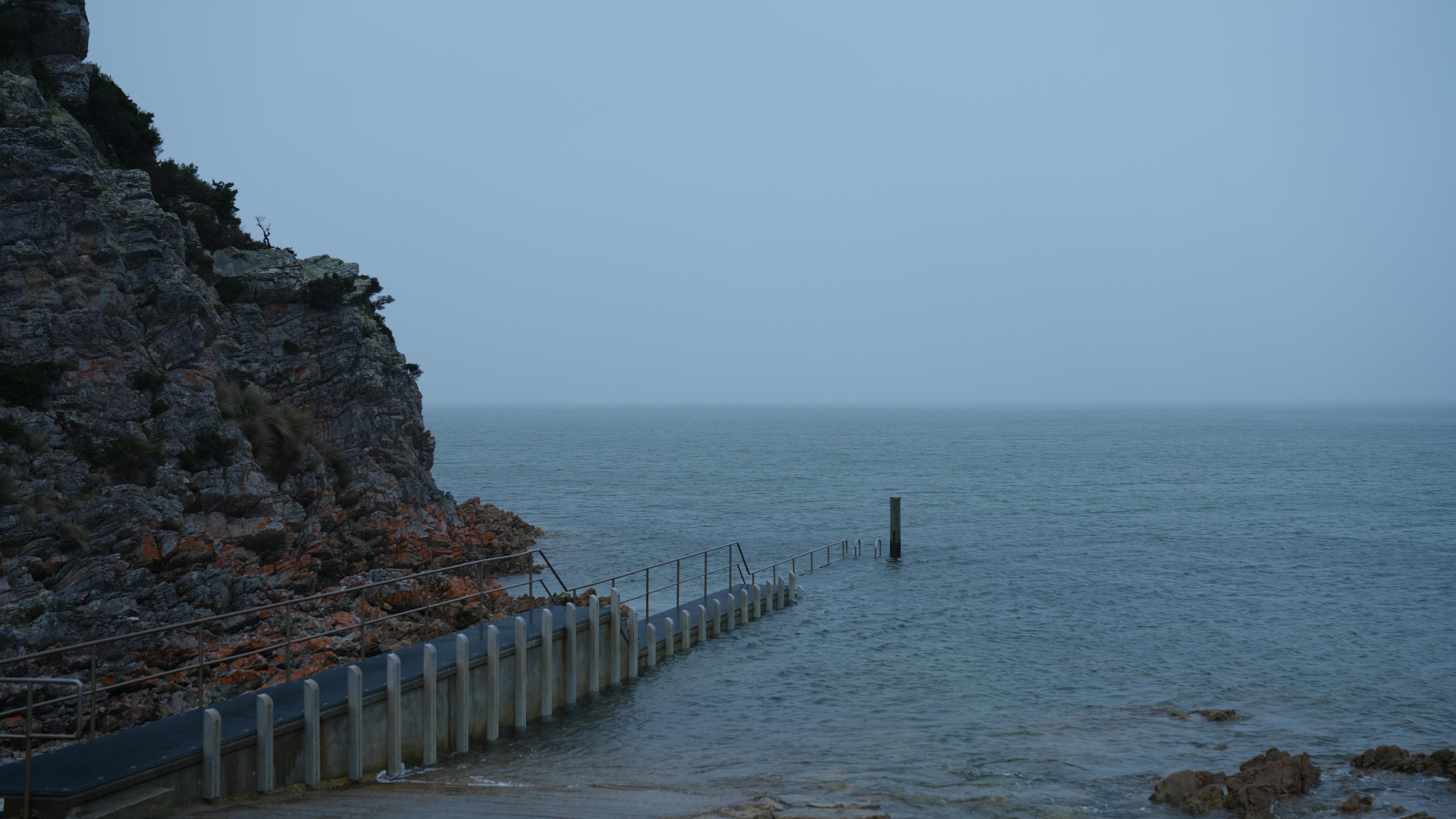 A rocky cliffside and jetty, looking out to the water on a foggy day.