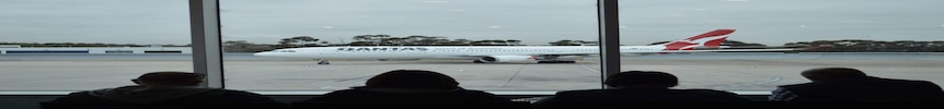 一架澳航飞机在阴天沿着跑道滑行，坐在里面的乘客在一旁观看。
