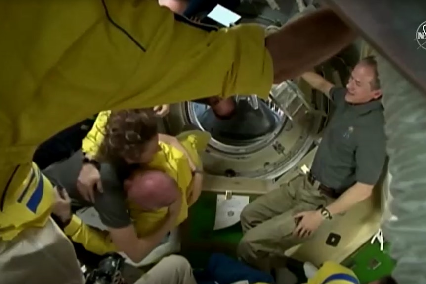 Cosmonaut in yellow hugs another floating in space. 