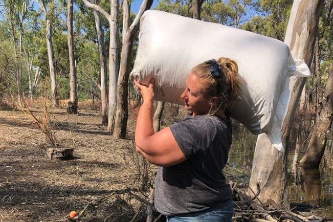 A woman with a bag of animal feed on her shoulder. 