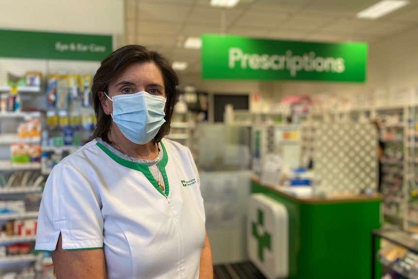 Una mujer enmascarada se encuentra en una farmacia.