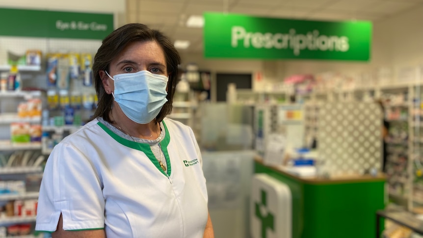 A masked and serious Helen O'Byrne stands in a pharmacy.