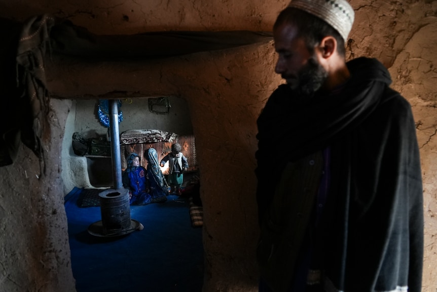 A man stands by a doorway with several children in the next room. 