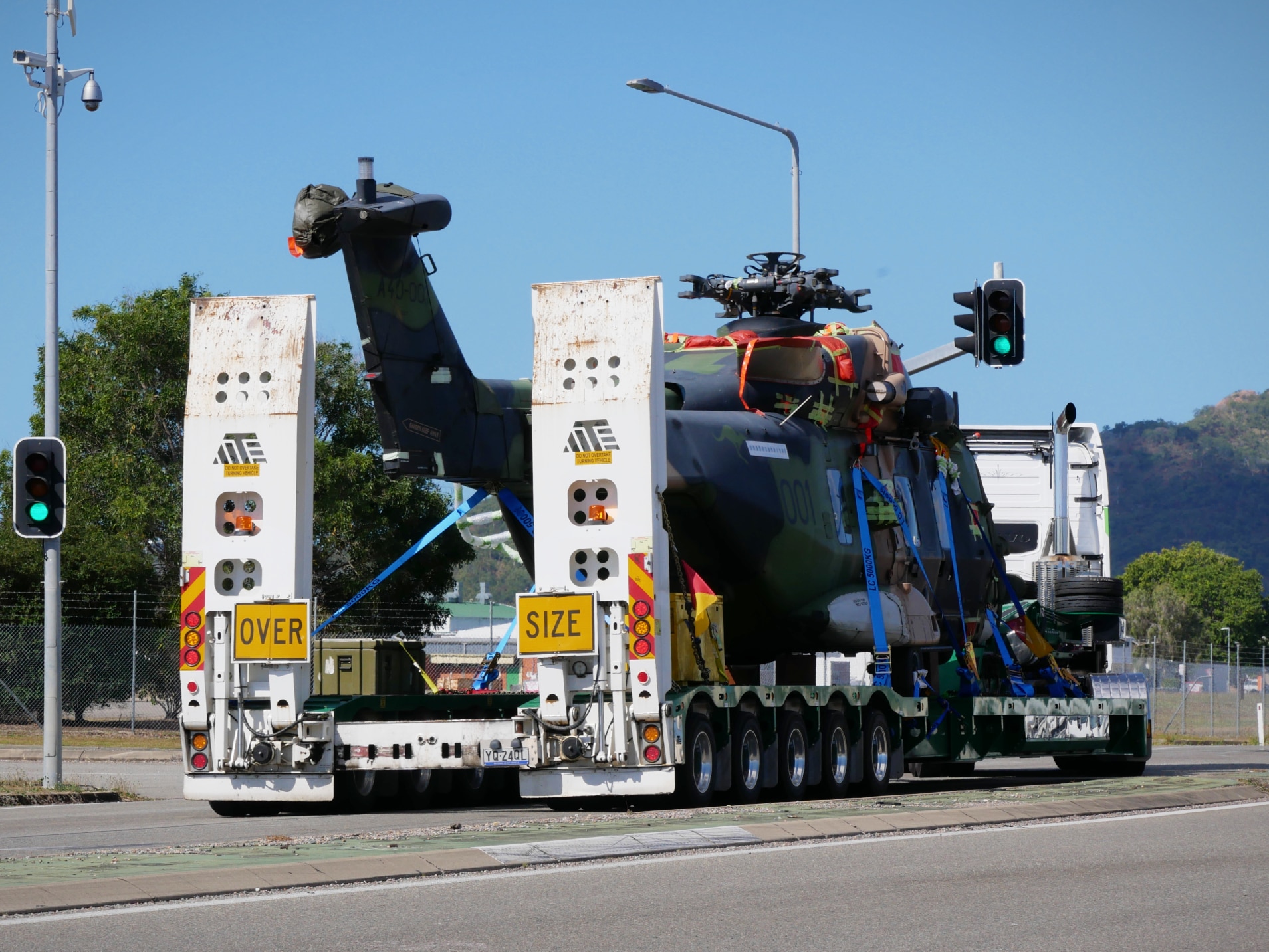 A military helicopter on the back of a large truck with an 'over size' sign