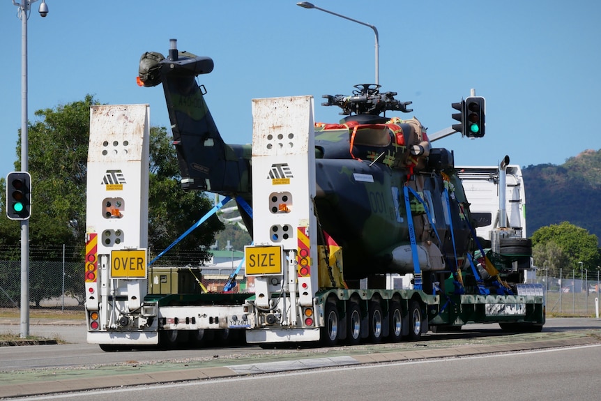 A military helicopter on the back of a large truck with an 'over size' sign
