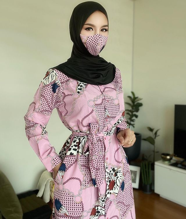 一位年轻女子穿着粉红色图案连衣裙和配套面具，头戴黑色头巾，时尚地披在肩上