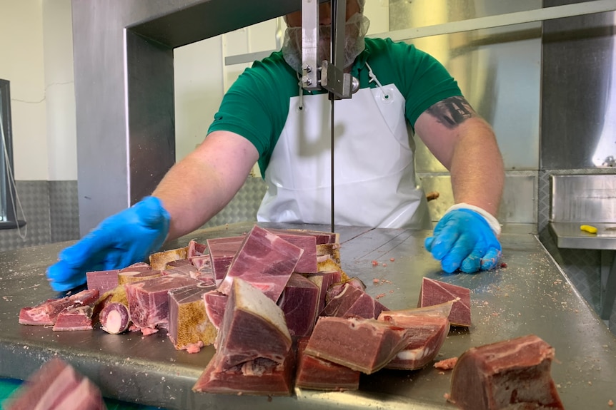 A man chops up meat on a stainless steel bench.