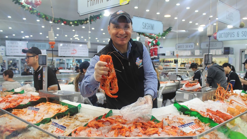 Man holds out prawns over a counter filled with seafood at the Sydney Fish Market