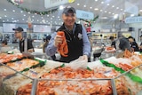 Man holds out prawns over a counter filled with seafood at the Sydney Fish Market