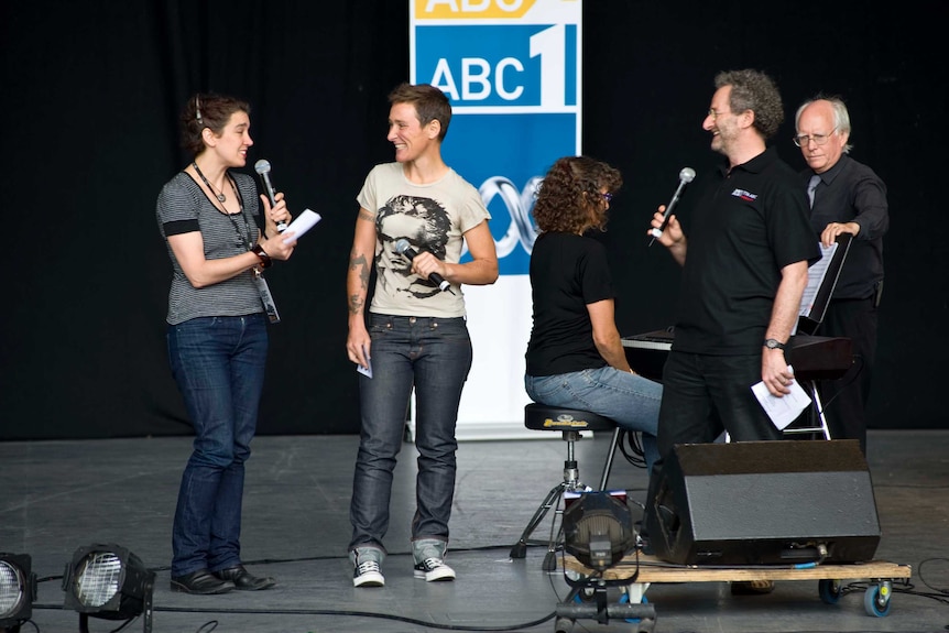 Faine on stage holding microphone with two other women.