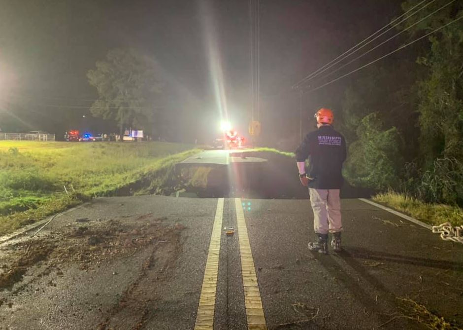 A worker looks on at a washed out road.