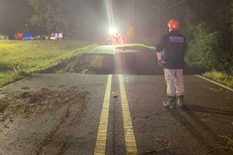 A worker looks on at a washed out road.