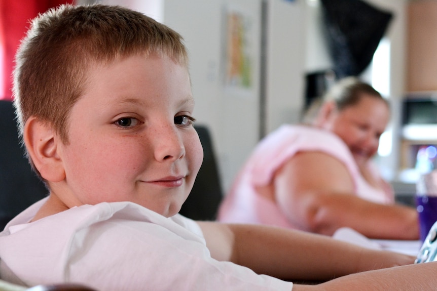 Eight-year-old Emilio looks sideways at the camera, while Belinda is smiling in the background.