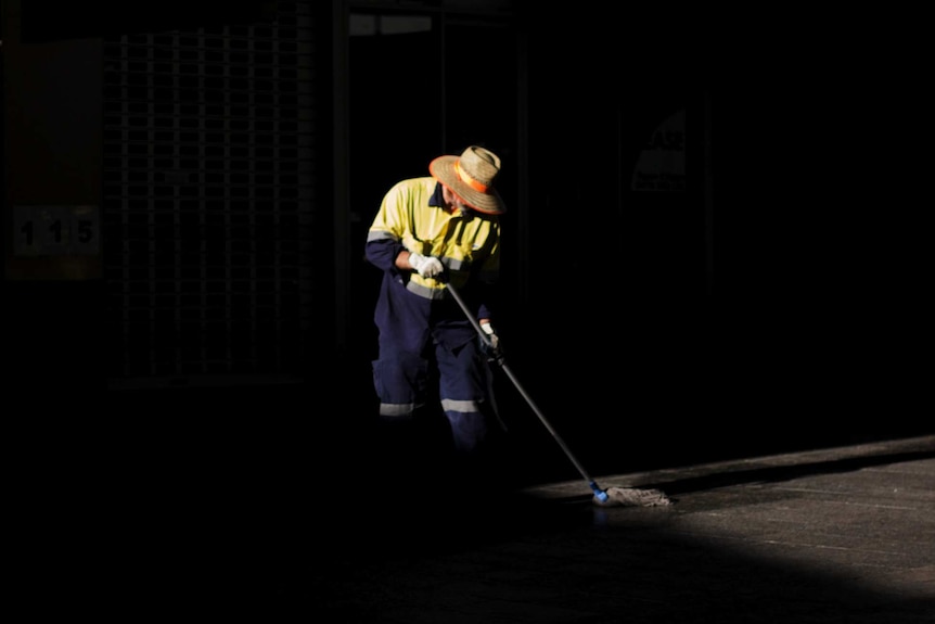 A person wearing high-visibility clothing sweeps the street.