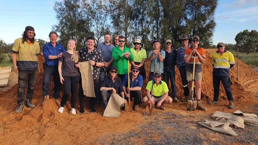 A group of people in work clothes stand in front of a mountain of dirt smiling at the camera.