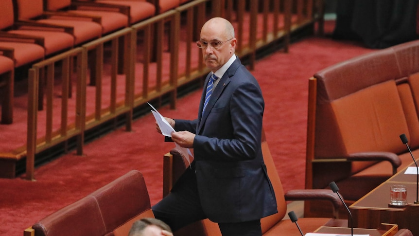 A bald man in a suit and glasses walks in the Senate chamber.