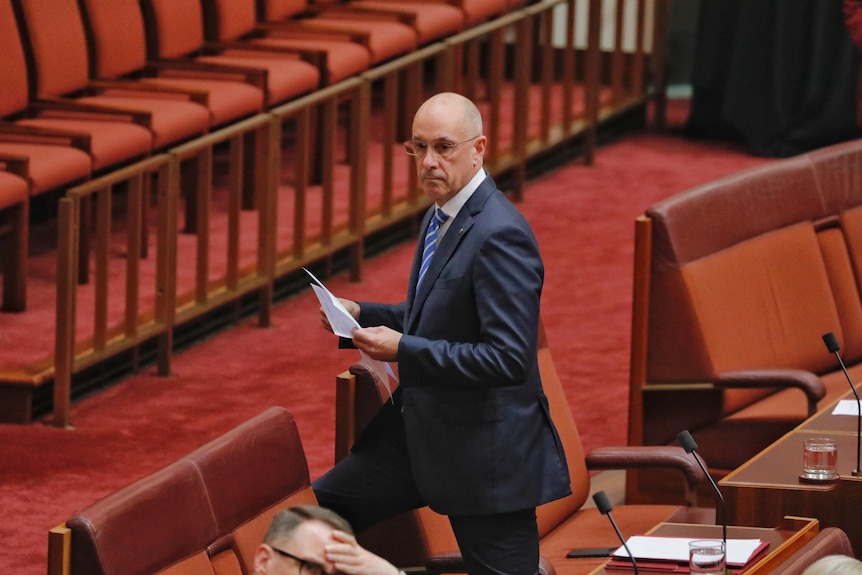 A bald man in a suit and glasses walks in the Senate chamber.