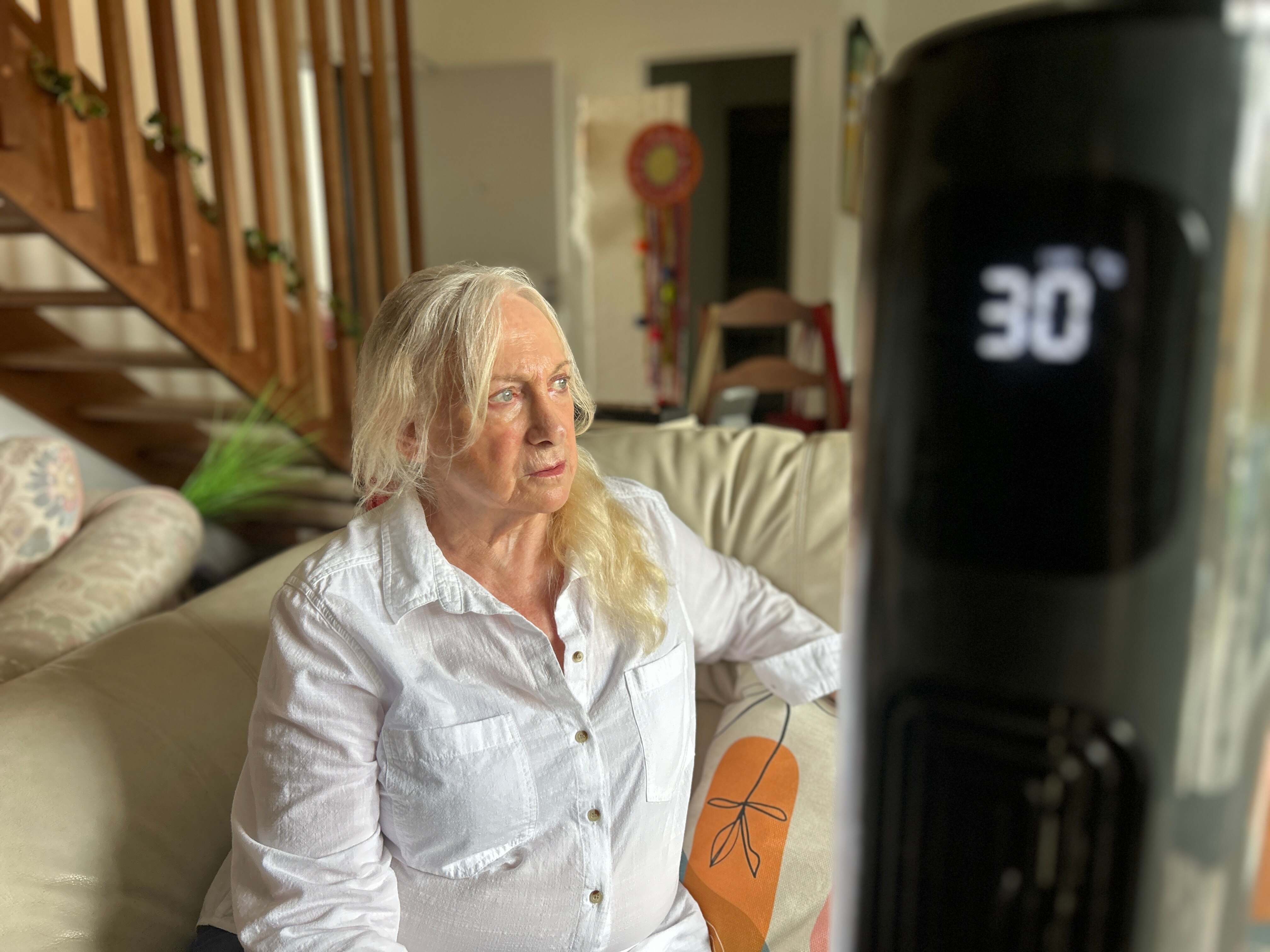 An older woman with white hair sits on a couch. A temperature gauge in the foreground read 30 degrees Celsius.