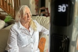 An older woman with white hair sits on a couch. A temperature gauge in the foreground read 30 degrees Celsius.