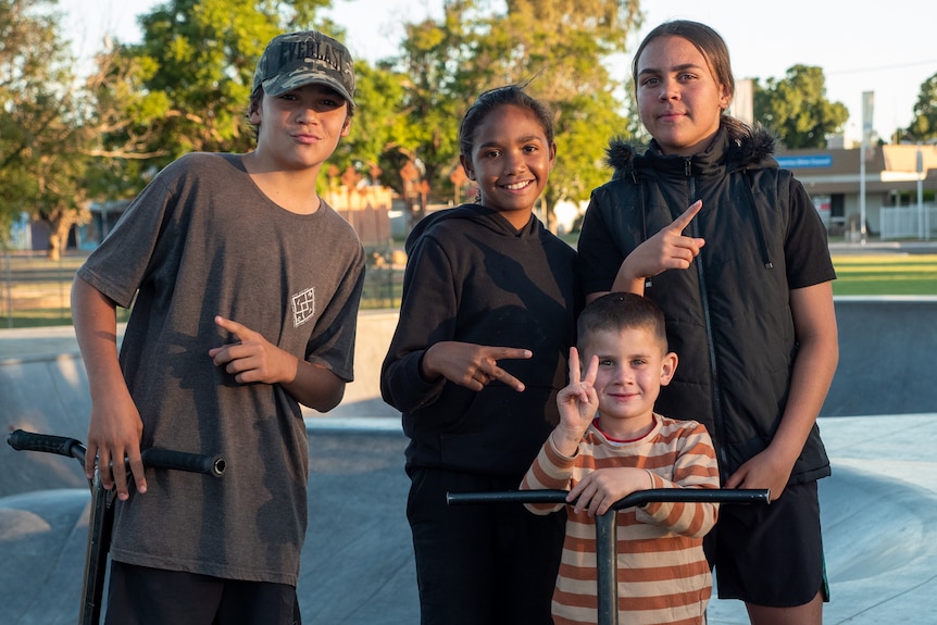 Four kids stand by their scooters at the skate bowl in the park