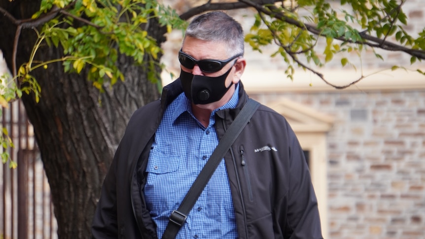 A man wearing a blue shirt, sunglasses and a black face mask