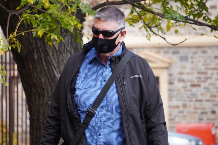 A man wearing a blue shirt, sunglasses and a black face mask