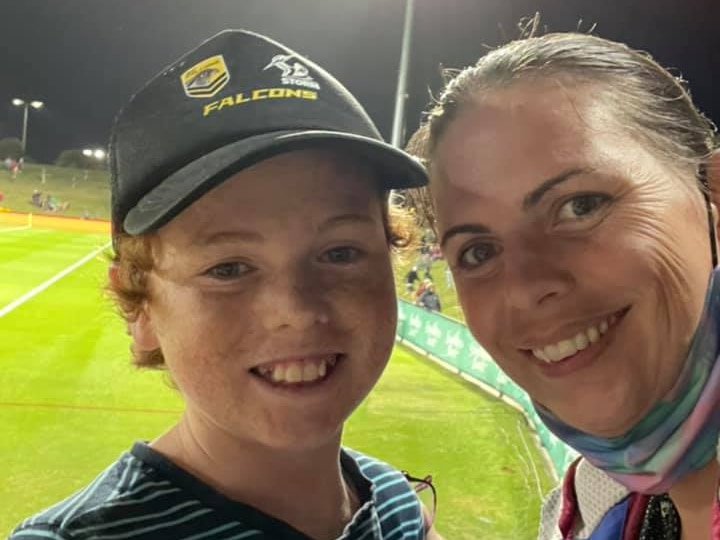 A boy and woman smiling for the camera with a football field in the background