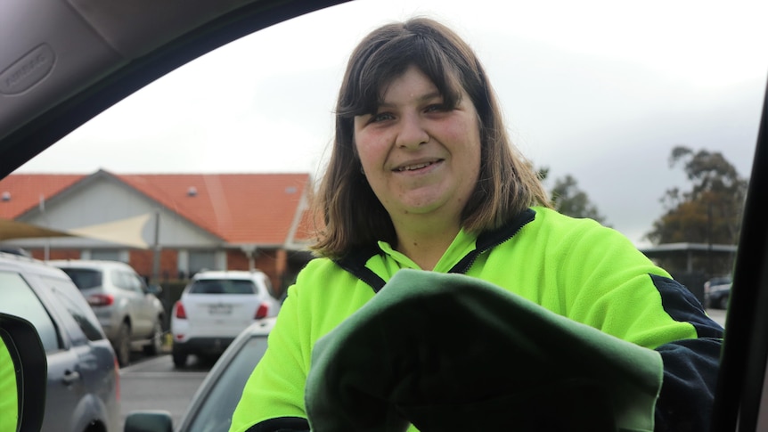 Woman in fluro top washes car window. Shot taken from inside the car.