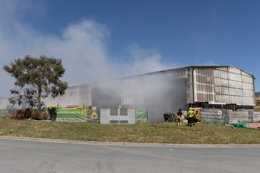 Smoke rises from the blackened warehouse, and some recycling products litter the ground.