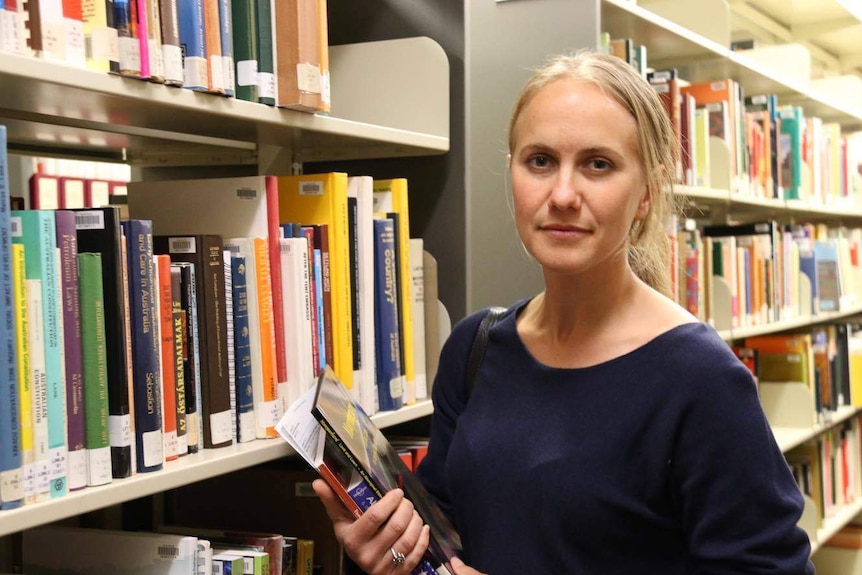 Katrina Olsen holds books in a library.