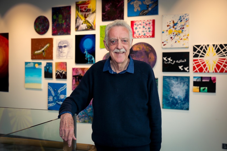 A man poses for a photo in front of a wall full of colourful artworks