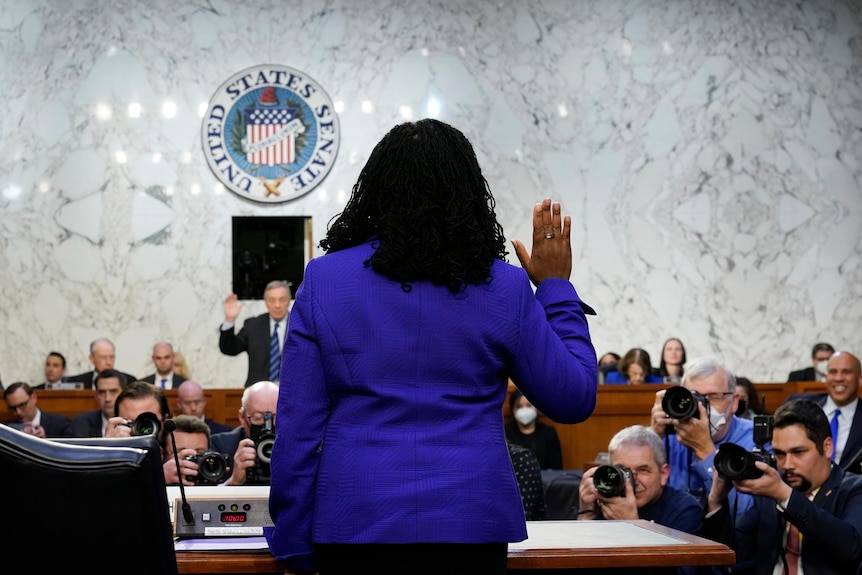 Ketanji Brown Jackson faces away from the camera holding her hand up during day one of her confirmation hearing