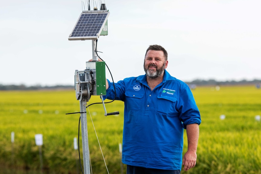 A man standing n a rice field with water saving technology including monitors and sensors.